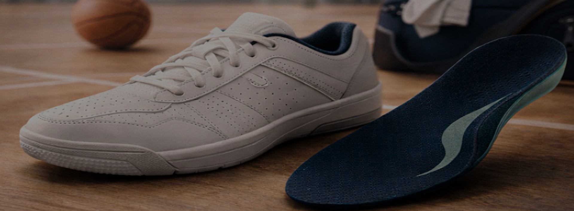 White basketball training shoe beside a custom orthotic insole on an indoor basketball court designed for comfort, arch support, and athletic performance.